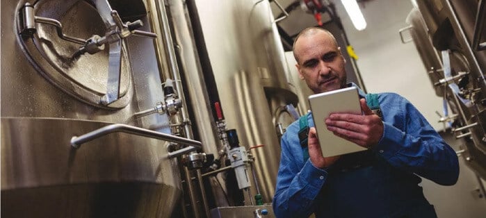 Brewer uses a tablet in a warehouse with adult beverage equipment to increase brewery operational efficiency