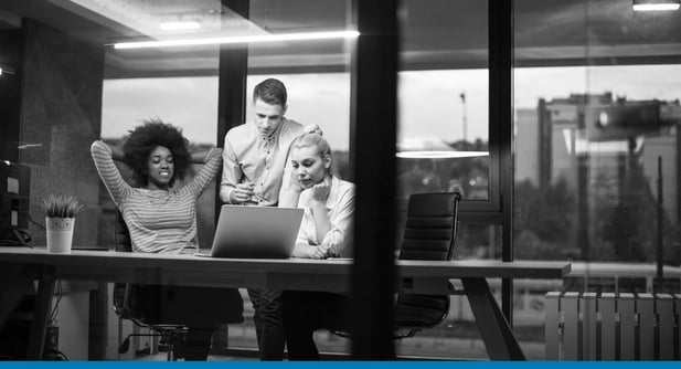 Two businesswomen and a businessman look at a laptop together, reading a guide about how to choose an ERP system