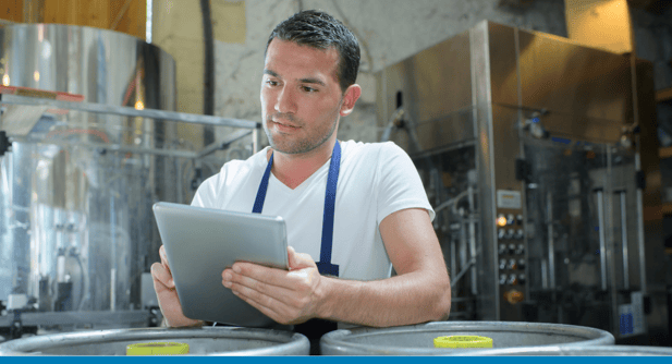 man examines a tablet with brewing and distilling equipment in the background