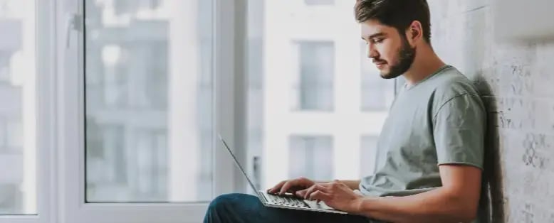 Person sitting on the floor near a large window, reading an ERP blog on a laptop